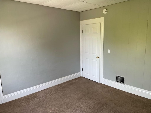 spare room with baseboards, dark colored carpet, a paneled ceiling, and visible vents