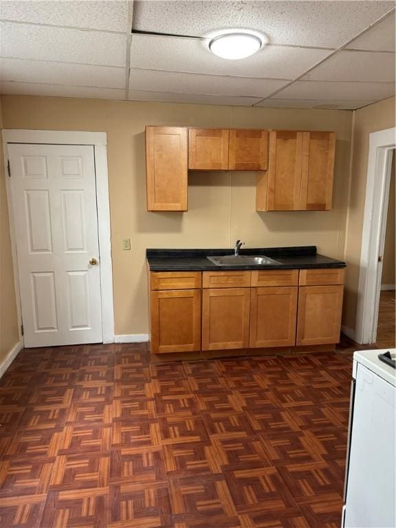 kitchen featuring dark countertops, a sink, stove, a paneled ceiling, and baseboards