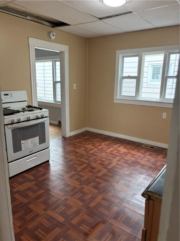 kitchen with baseboards, white gas stove, a paneled ceiling, and visible vents