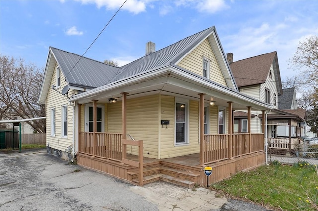 view of front of house with covered porch, a chimney, and metal roof
