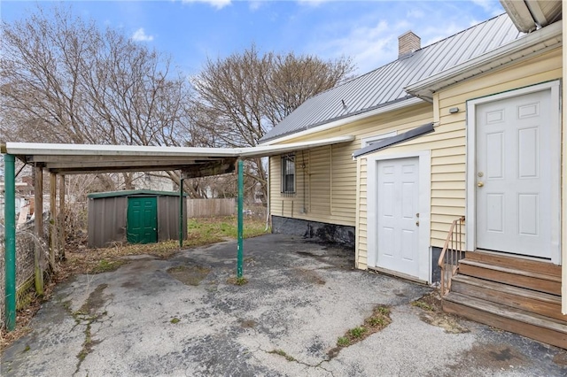view of patio / terrace with a carport, fence, an outdoor structure, a shed, and entry steps