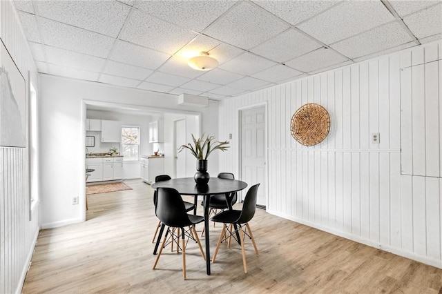 dining room featuring baseboards, a drop ceiling, and light wood-style flooring