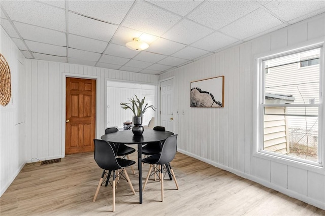 dining area with baseboards, a drop ceiling, and light wood-style flooring