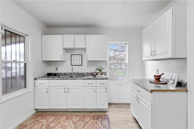 kitchen featuring a sink, baseboards, light wood-style floors, and white cabinetry