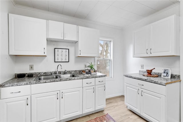kitchen with a sink, white cabinets, light wood-style floors, and ornamental molding