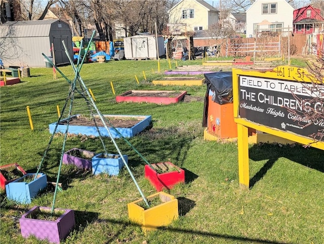 view of play area featuring fence, a yard, a vegetable garden, a storage shed, and an outbuilding