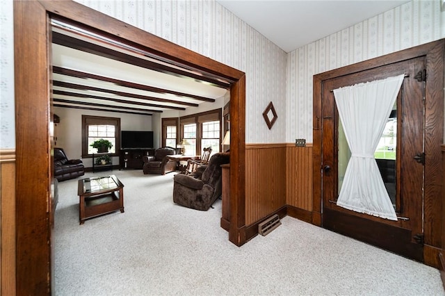 carpeted living room with beamed ceiling, wainscoting, and wallpapered walls