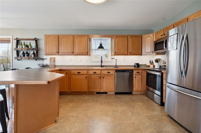 kitchen featuring decorative backsplash, a peninsula, a kitchen bar, a sink, and appliances with stainless steel finishes