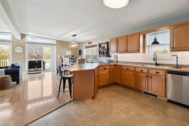 kitchen featuring plenty of natural light, backsplash, stainless steel dishwasher, a sink, and a peninsula