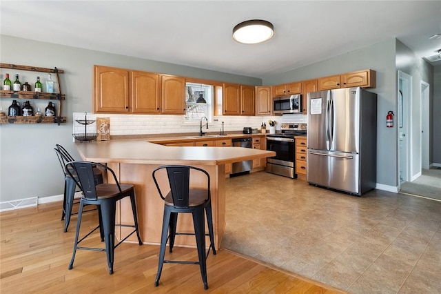 kitchen featuring a peninsula, a kitchen breakfast bar, tasteful backsplash, a sink, and stainless steel appliances