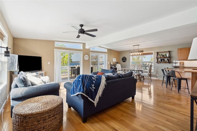 living room featuring light wood-style floors, baseboards, ceiling fan, and a healthy amount of sunlight