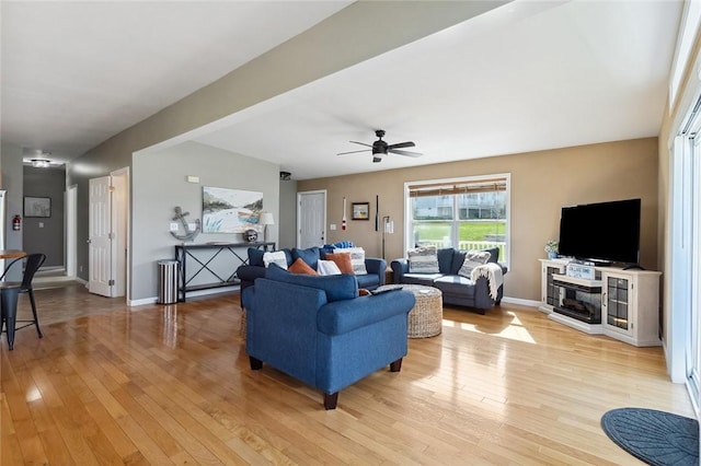 living area with baseboards, a ceiling fan, and light wood-style flooring