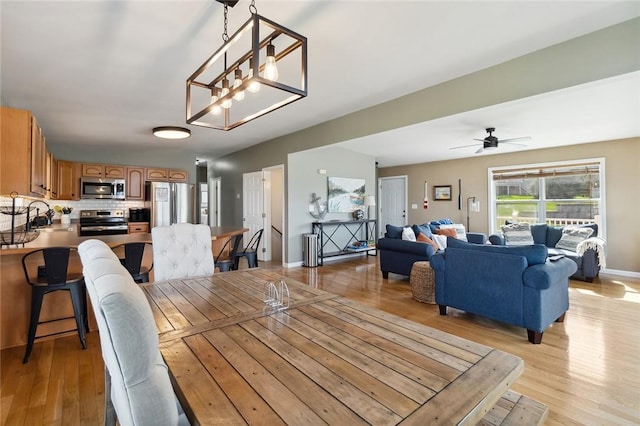 dining space featuring baseboards, light wood-style flooring, and ceiling fan with notable chandelier