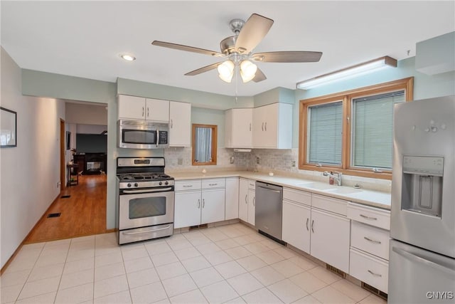 kitchen featuring decorative backsplash, light countertops, white cabinets, a sink, and appliances with stainless steel finishes