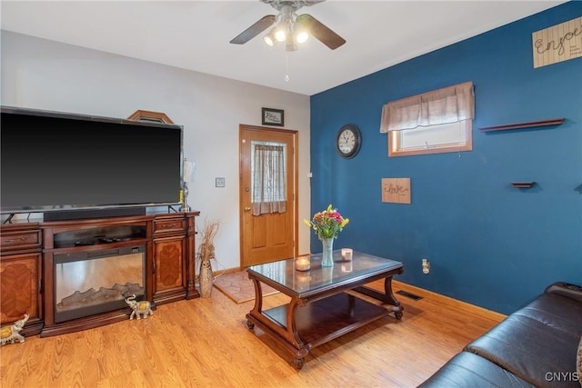 living room featuring light wood-style floors, baseboards, a ceiling fan, and visible vents