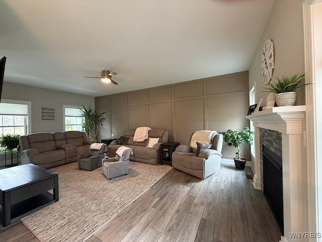 living room featuring a tiled fireplace, dark wood-type flooring, a decorative wall, and a ceiling fan