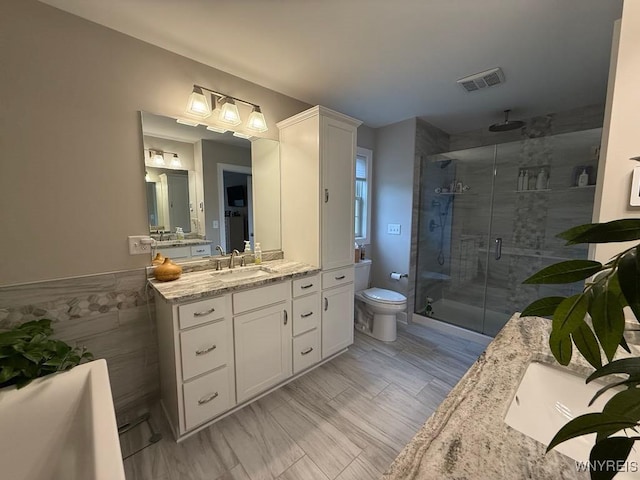 full bathroom with toilet, tile walls, visible vents, a shower stall, and vanity