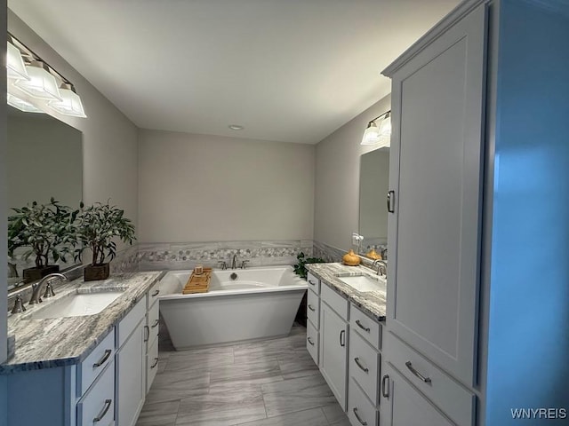 full bathroom with marble finish floor, a freestanding tub, two vanities, and a sink