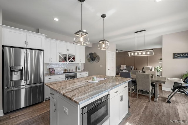 kitchen featuring decorative backsplash, a center island, white cabinets, light stone countertops, and appliances with stainless steel finishes