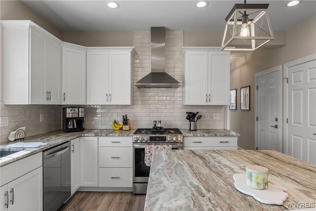 kitchen with appliances with stainless steel finishes, wall chimney exhaust hood, white cabinets, wood finished floors, and recessed lighting
