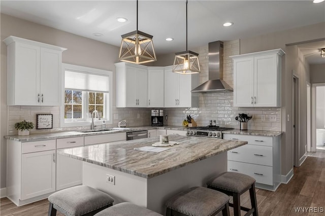 kitchen featuring wall chimney exhaust hood, a sink, a kitchen bar, white cabinetry, and recessed lighting