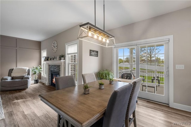 dining space featuring baseboards, light wood-style floors, and a lit fireplace