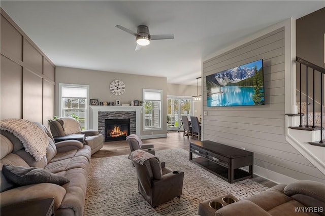 living area with wood finished floors, a stone fireplace, a ceiling fan, and stairs