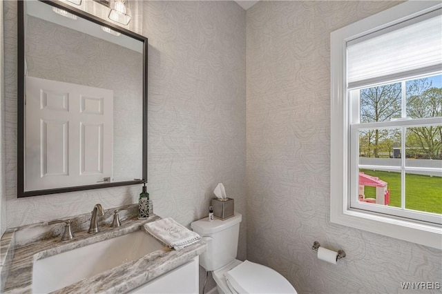 bathroom with toilet, wallpapered walls, and vanity