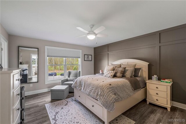 bedroom featuring dark wood finished floors, baseboards, ceiling fan, and a decorative wall