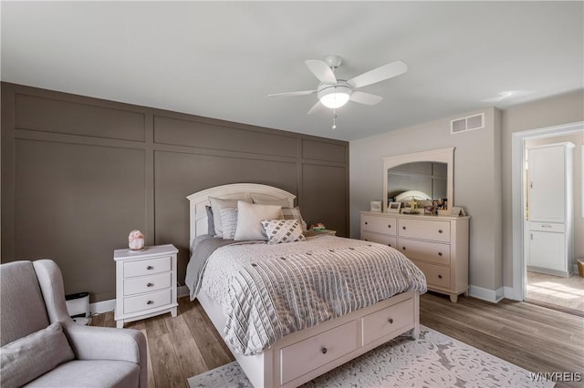 bedroom with light wood finished floors, visible vents, and a decorative wall