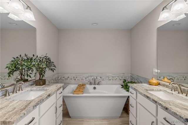 bathroom featuring two vanities, tile walls, a freestanding tub, and a wainscoted wall