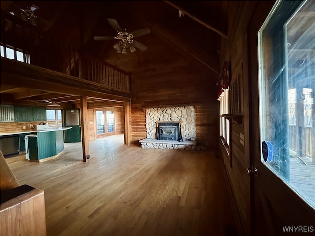 unfurnished living room featuring high vaulted ceiling, light wood finished floors, a ceiling fan, and wood walls