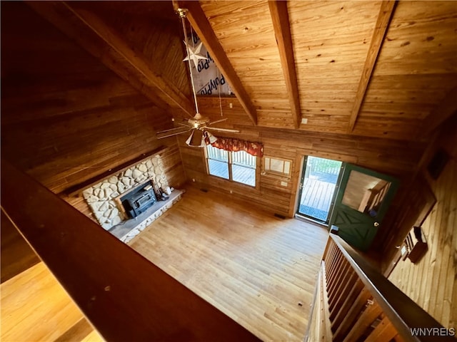 unfurnished living room with wood walls, wood finished floors, a stone fireplace, wood ceiling, and a ceiling fan