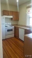 kitchen featuring brown cabinetry, light countertops, under cabinet range hood, and white appliances