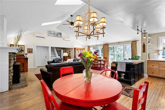 dining area with a stone fireplace, light wood-style flooring, stairs, a skylight, and a wall mounted AC
