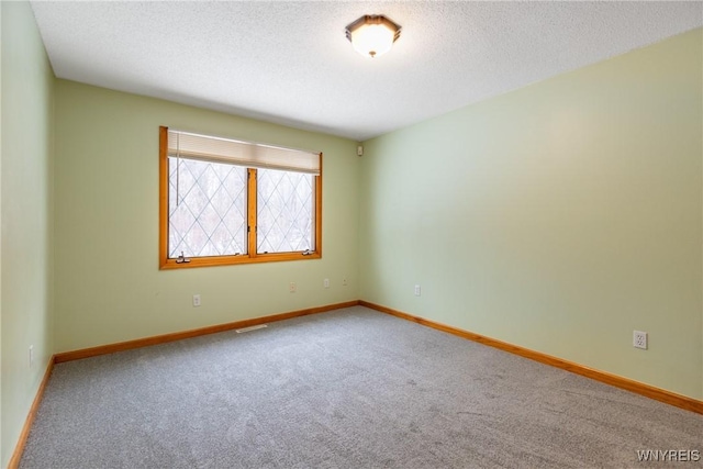 carpeted spare room featuring a textured ceiling, visible vents, and baseboards