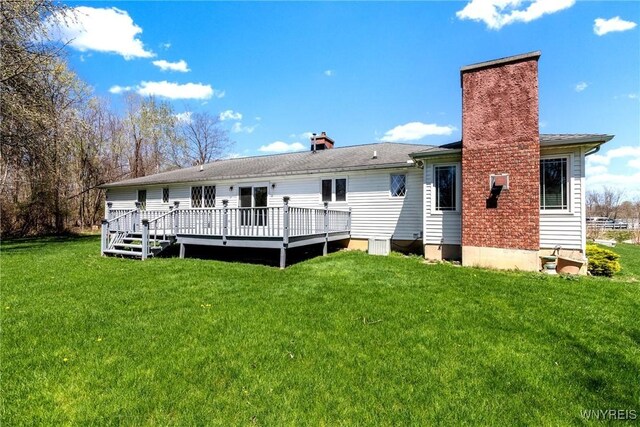 rear view of property featuring a chimney, a yard, and a wooden deck