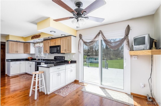 kitchen featuring a peninsula, dark countertops, light wood-style flooring, and black appliances