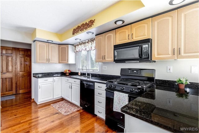kitchen with dark stone countertops, a sink, black appliances, and light wood-type flooring