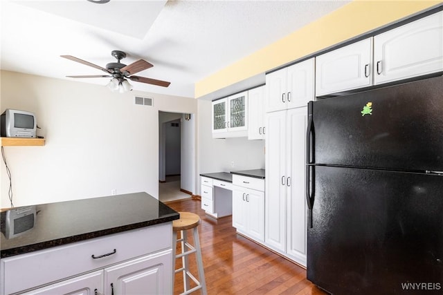 kitchen with white cabinets, dark countertops, ceiling fan, freestanding refrigerator, and wood finished floors