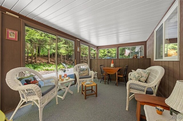 sunroom featuring carpet floors, outdoor dining space, and wooden walls