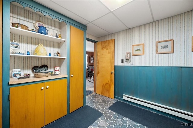 interior space featuring wainscoting, a baseboard heating unit, and a drop ceiling