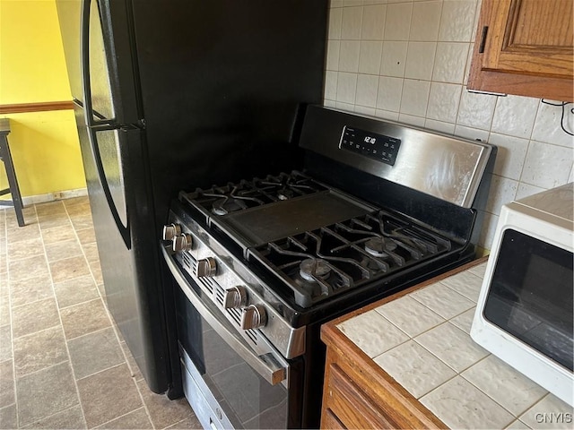 kitchen featuring brown cabinets, gas stove, baseboards, decorative backsplash, and white microwave
