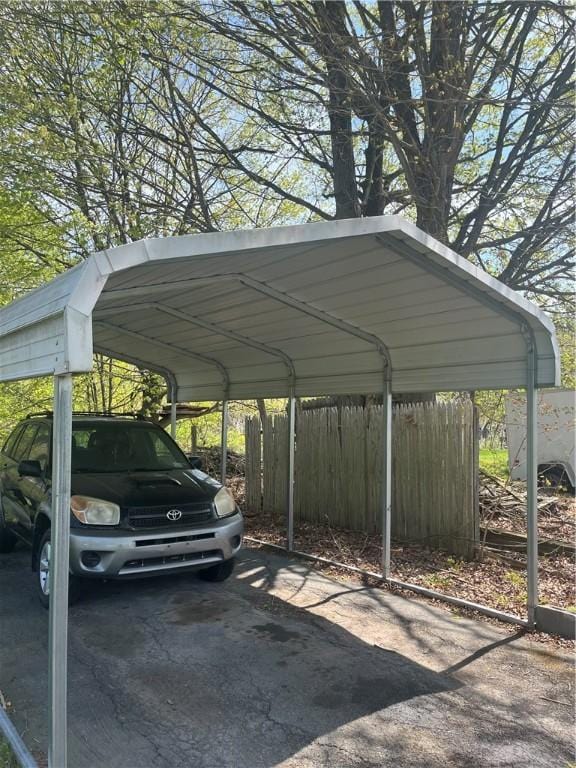view of vehicle parking featuring fence and a carport