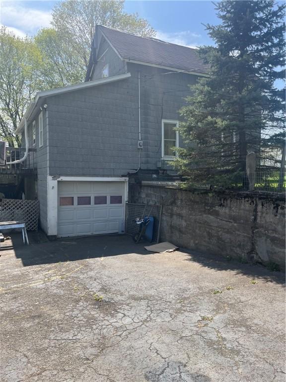 view of side of property featuring a garage, concrete block siding, aphalt driveway, and fence