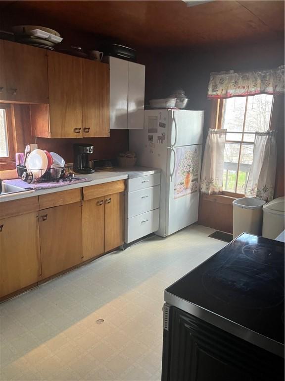 kitchen with brown cabinets, light countertops, freestanding refrigerator, light floors, and range with electric stovetop