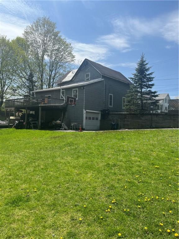 rear view of property featuring an attached garage, a yard, and a deck