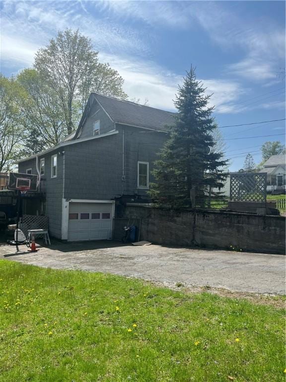 view of side of property featuring a yard, an attached garage, fence, and aphalt driveway