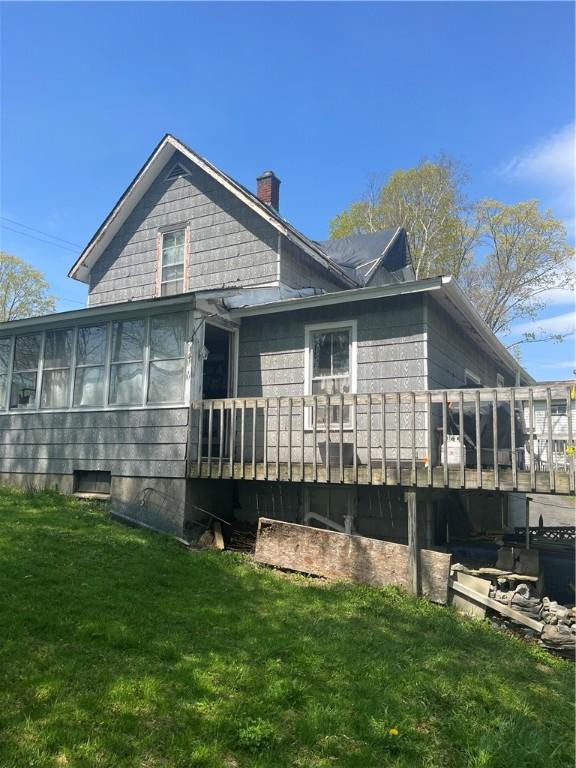 view of side of home featuring a sunroom, a chimney, a yard, and a deck