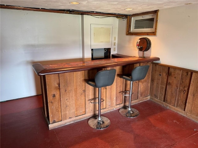 bar with a dry bar, a textured ceiling, a wainscoted wall, and wood walls